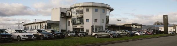 Das Bild zeigt das KBM Mercedes-Benz Autohaus in Limburg im Hintergrund, flankiert von hochwertigen Mercedes-Benz Fahrzeugen, die auf dem Parkplatz geparkt sind.